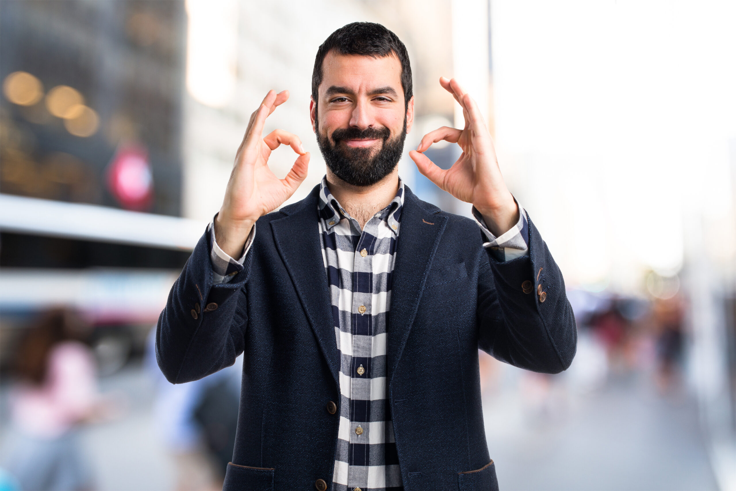 A cheerful man in a navy blazer gives an "OK" gesture with both hands, symbolizing quality and excellence in facility management.