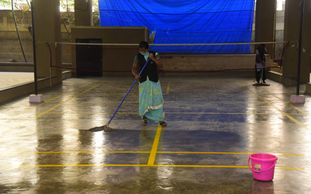 Woman mopping a badminton court as part of facility management services, with another worker and cleaning tools visible in the background.